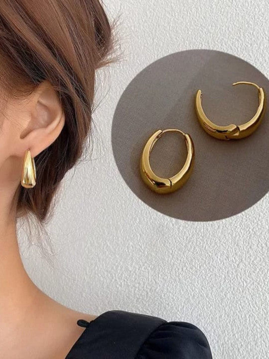 Gold plated oval hoop earrings displayed on model, showcasing their chic huggie style and polished finish.