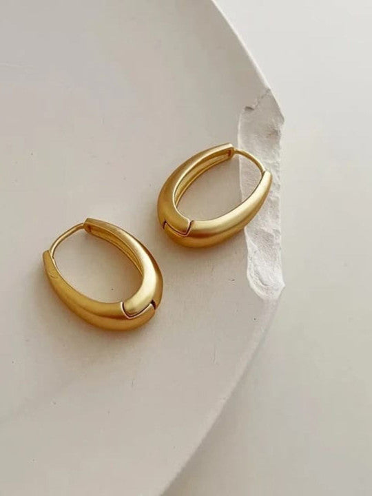 Gold plated oval hoop earrings on a white plate, showcasing their chunky huggie style and luxurious finish.