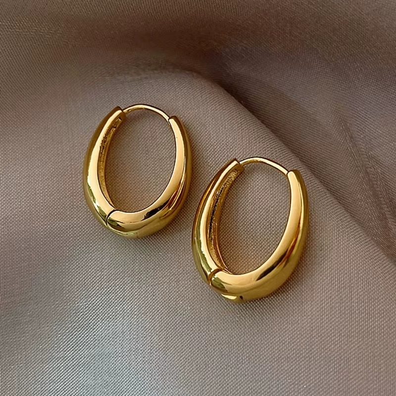 Gold plated oval hoop earrings on soft fabric, showcasing a chic chunky huggie design and high-polish finish.
