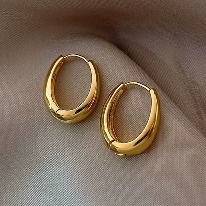 Gold plated oval hoop earrings on soft fabric, showcasing a chic chunky huggie design and high-polish finish.