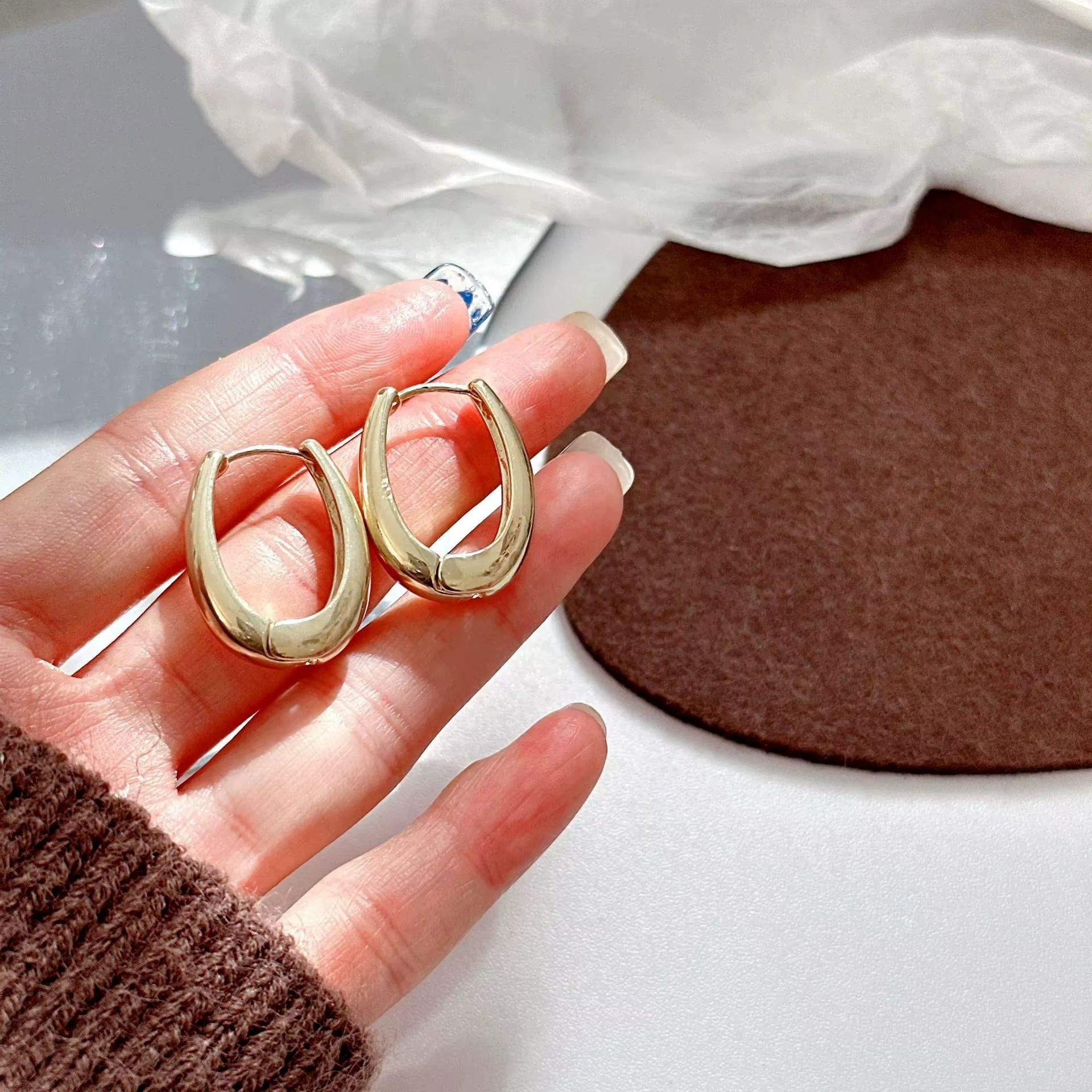 Gold plated oval hoop earrings in a hand, showcasing their chunky huggie style and high-polish finish.