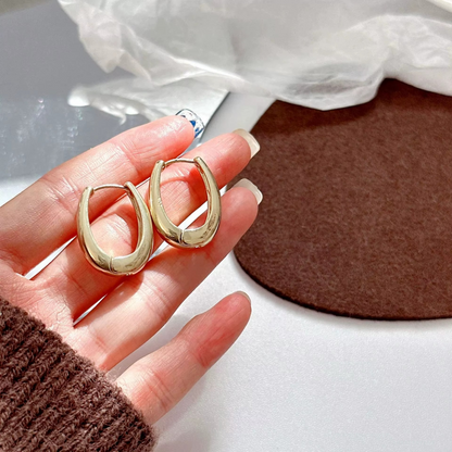 Gold plated oval hoop earrings in a hand, showcasing their chunky huggie style and high-polish finish.